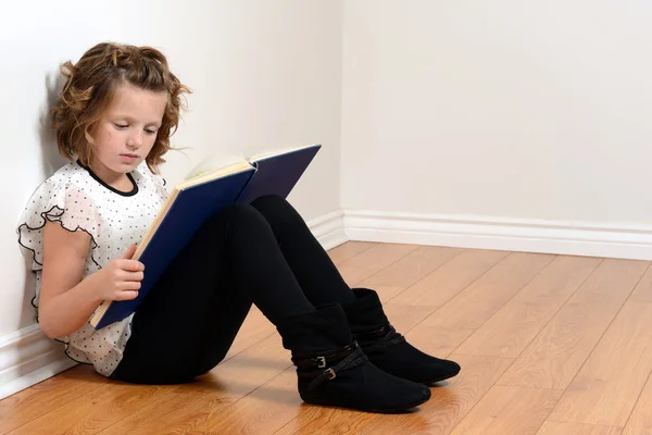 Young girl leaning on wall reading book — Stock Photo, Image