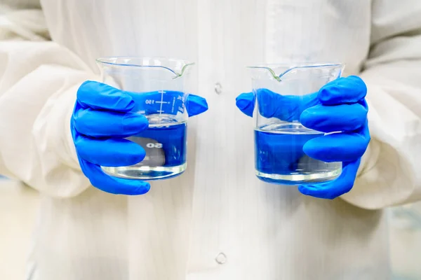 Person Lab Coat Holding Two Beakers Clear Liquids — Stockfoto