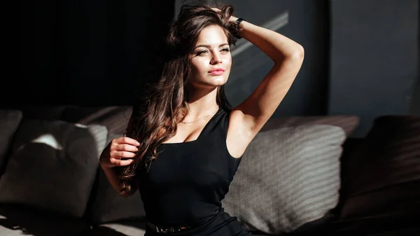 Portret van een sexy brunette in een zwarte jurk op een donkere achtergrond. meisje neemt uit haar jurk langzaam in de slaapkamer — Stockfoto