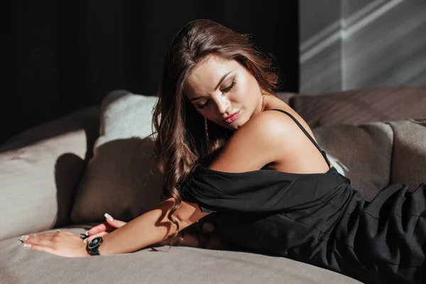 Porträtt av en sexig brunett i svart klänning på en mörk bakgrund. flicka tar av sig klänningen långsamt i sovrummet — Stockfoto