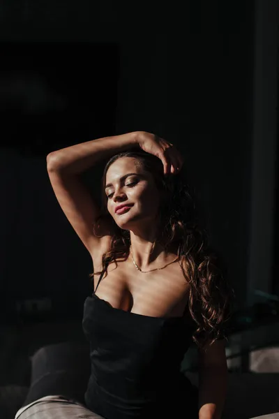 Ritratto di una bruna sexy vestita di nero su sfondo scuro. ragazza si toglie il vestito lentamente in camera da letto — Foto Stock