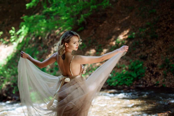 Een mooi meisje in een jurk staat bij de rivierbedding in de natuur buiten — Stockfoto