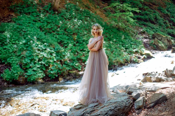 Krásná dívka v šatech stojí v blízkosti koryta řeky v přírodě — Stock fotografie