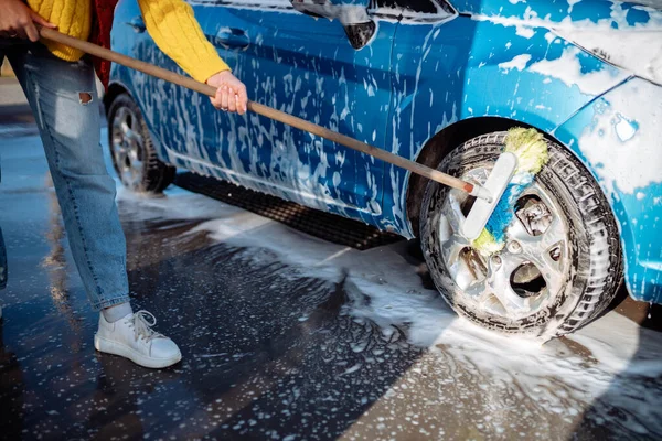 Menina bonita lava o carro na lavagem de carro self-service. Apagando sujeira para o carro com uma escova — Fotografia de Stock