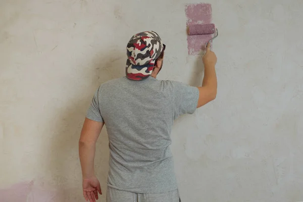 The rear view of a young adult man paints the wall with a roller. Repair in the house with their own hands — Stock Photo, Image