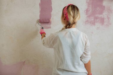 Yeni evin duvarını silindirli genç kadın boyuyor.