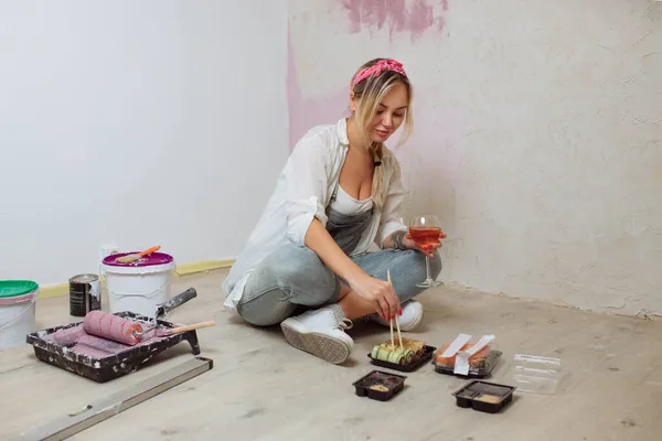 Sexy chica diseñadora come sushi en el sitio de construcción. pintor tiene almuerzo después del trabajo.Concepto de diseño de interiores y reparación de habitaciones — Foto de Stock