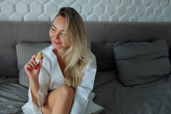 Frühstück im Haus. Ein sexy Mädchen im weißen Bademantel isst Makronen. Hotelurlaub — Stockfoto