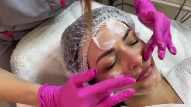 O cosmetologist aplica a espuma para lavar-se na cara de pacientes. Spa Cosmetologia — Vídeo de Stock