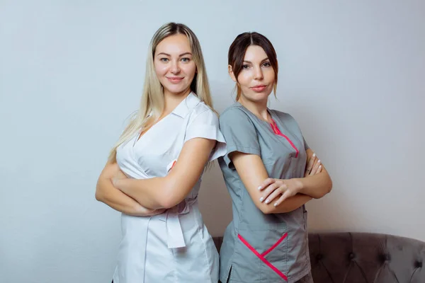 Duas mulheres sexy bonitas jovens cosmetologists colegas em branco roupas elegantes de pé e sorrindo. — Fotografia de Stock