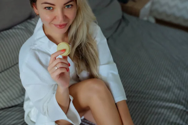 Close-up Petit déjeuner en intérieur.Une fille sexy en peignoir blanc mange macaron. Hôtel vacances — Photo