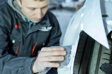 Kazadan sonra, boya yapmadan önce zımparalamak suretiyle araba gövdesini onarmak. Tamirci plastik macun kullanarak arabayı tamir ediyor ve sprey boyaya hazırlanıyor..