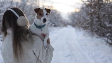 A girl in a snowy forest carries a dog Jack Rassell Terrier in her arms. Training and walking with pets