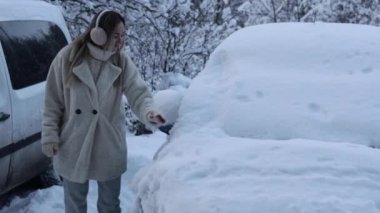 Clearing the car of snow. A young beautiful girl cleans snow from the windshield of a car. Harsh winter