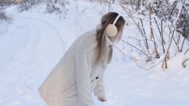 Girl in the winter walks and has fun in the fresh air. cheerful excited woman throws snow and rejoices in flying snowflakes on a sunny frosty winter day — Stockvideo