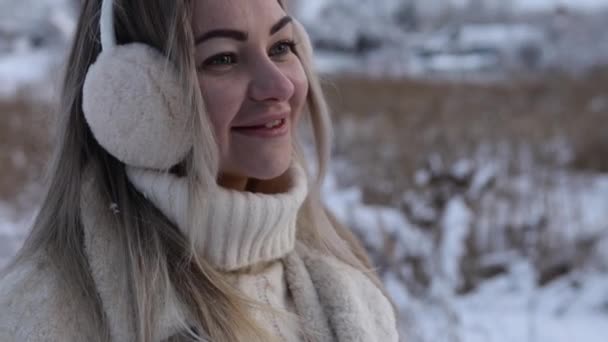 Close-up portrait of a Cute young Caucasian girl in fur headphones and a white winter sweater. Winter walk in the snowy forest. — Stockvideo