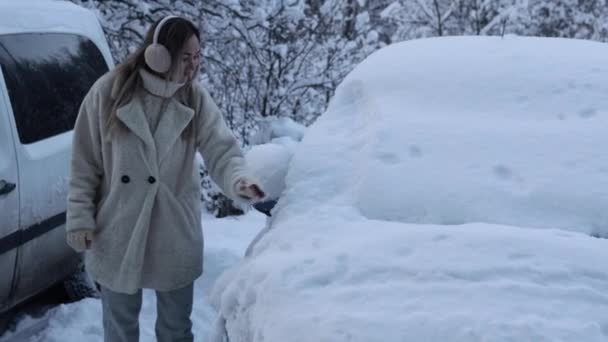 雪の車を掃除する。若い美しい少女が車のフロントガラスから雪をきれいにします。厳しい冬 — ストック動画