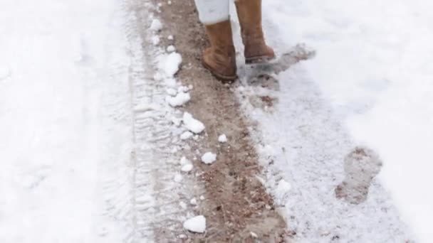 Κοντινό πλάνο ενός κοριτσιού με μπότες περπατά κατά μήκος ενός καταιονισμένου μονοπατιού σε χειμερινό χιονισμένο καιρό. Εργασίες αφαίρεσης χιονιού — Αρχείο Βίντεο