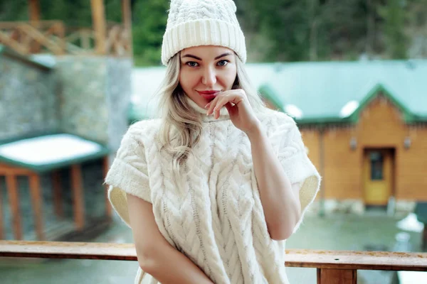 Retrato de uma menina bonita em um chapéu branco e suéter na rua na varanda. Roupas quentes de inverno — Fotografia de Stock