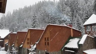 Dağlarda çam ağaçlarıyla çevrili ahşap kulübeler. Kar yağarken ahşap bir otelin kışın dış tarafında..