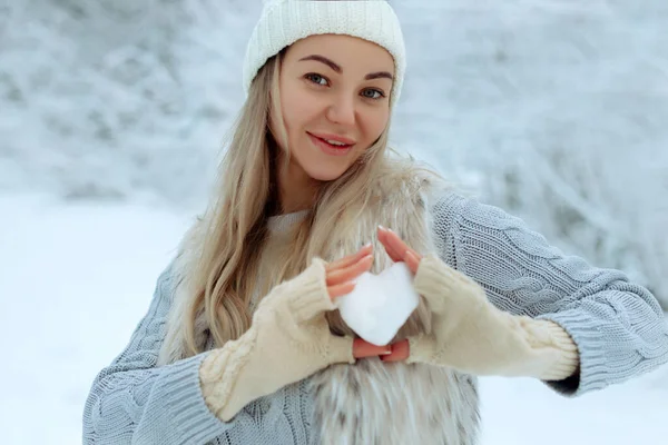 Eu gosto do inverno. Retrato de uma menina feliz segurando um coração nevado em sua mão durante o inverno. Dia dos Namorados. — Fotografia de Stock