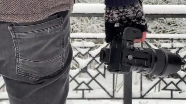手袋をはめた手のカメラ雪の冬のクローズアップを保持しています。写真家は雪が降るベルトのレベルでカメラを保持します。 — ストック動画