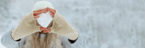 Banner Close-up Corazón de nieve en las manos con guantes de punto sobre el fondo de la cubierta de nieve. Día de San Valentín —  Fotos de Stock