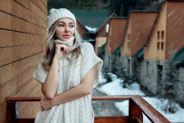 Retrato de uma menina bonita em um chapéu branco e suéter na rua na varanda. Roupas quentes de inverno — Fotografia de Stock