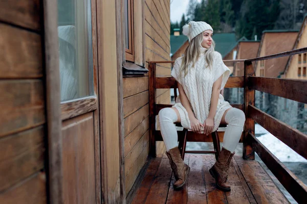 Ένα σέξι κορίτσι με λευκό πουλόβερ και κάλτσες στο μπαλκόνι θαυμάζει την ομορφιά της φύσης. μάλλινα ρούχα και καπέλο σε μια όμορφη ξανθιά — Φωτογραφία Αρχείου