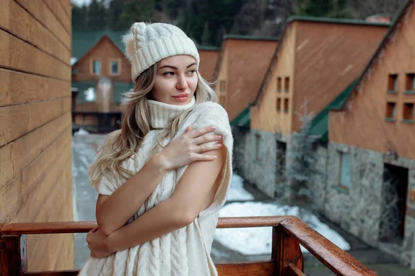 Retrato de una hermosa chica en un sombrero blanco y suéter en la calle en el balcón. Ropa cálida de invierno —  Fotos de Stock