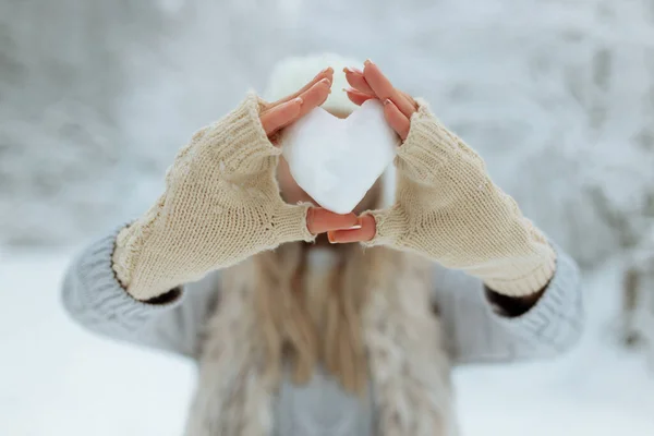 Close-up menina segura um coração nevado na frente dela em luvas — Fotografia de Stock