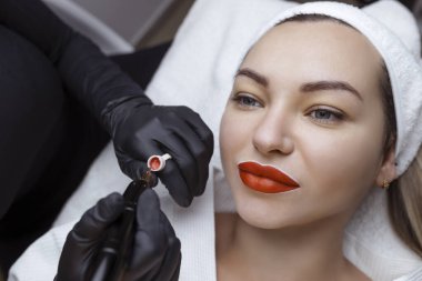 Kozmetik uzmanı bir kadının yüzüne kalıcı makyaj yapıyor. Uzman, hastaların dudaklarına yakın plan dövme uygular.