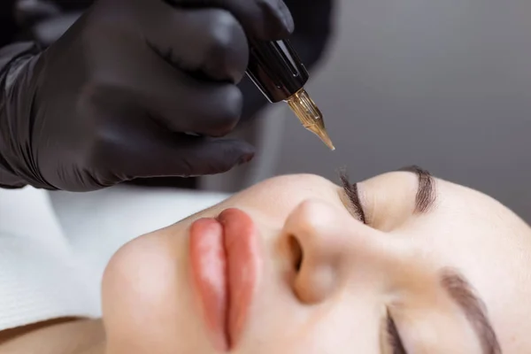 Close-up of a woman, in a beauty salon with her eyes closed, a cosmetologist makes permanent eyeliner makeup. Professional in black gloves and with a special too