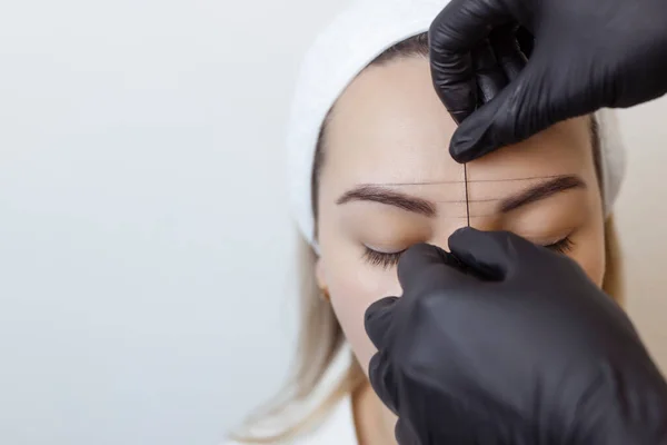 Eyebrow tattooing .Permanent eyebrow makeup master applies the contour with thread on the clients eyebrow