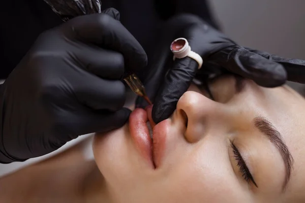 Stały makijaż nagich ust. Kosmetolog w salonie wykonuje zabieg tatuażu z zbliżeniem na maszynę do tatuażu — Zdjęcie stockowe