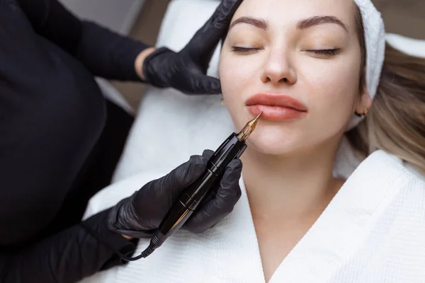 El cosmetólogo hace el maquillaje permanente a la persona de mujer. Especialista aplica un tatuaje en los labios de los pacientes de cerca — Foto de Stock