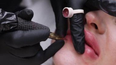 Bir kadının dudaklarına kalıcı makyaj dövmesi kırmızısı sürme işlemi. Dövme aleti ile boya uygulayan bir uzman