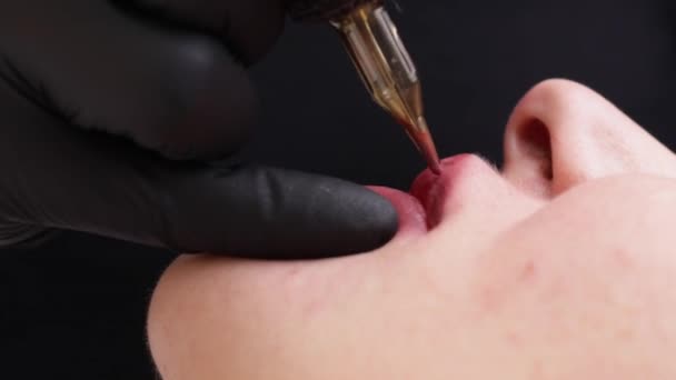 Τη διαδικασία της εφαρμογής μόνιμη τατουάζ μακιγιάζ κόκκινο χρώμα στα χείλη μιας γυναίκας. Ειδικός στην εφαρμογή χρωμάτων με εργαλείο τατουάζ — Αρχείο Βίντεο
