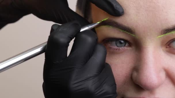La main d'un maquilleur en gants noirs applique une pâte à sourcils jaune sur le sourcil. Maquillage permanent élégant professionnel, teinte des sourcils. Gros plan. — Video