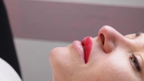 Jonge vrouw met permanente make-up op haar lippen in een kosmetologen salon. Permanente make-up tatoeage. trek een lijn met een rood lippotlood — Stockvideo
