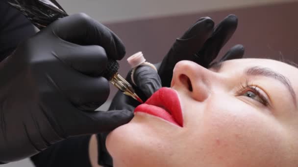 Le processus d'application de la couleur rouge de tatouage de maquillage permanent sur les lèvres d'une femme. Spécialiste appliquant de la peinture avec outil de tatouage — Video