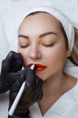  Kozmetik uzmanlarının salonunda dudaklarında kalıcı makyajı olan genç bir kadın. Kalıcı makyaj dövmesi. Beyaz dudak kalemiyle bir çizgi çiz