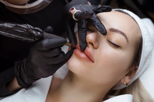 Stały makijaż nagich ust. Kosmetolog w salonie wykonuje zabieg tatuażu z zbliżeniem na maszynę do tatuażu — Zdjęcie stockowe
