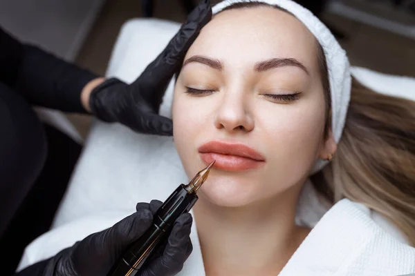El cosmetólogo hace el maquillaje permanente a la persona de mujer. Especialista aplica un tatuaje en los labios de los pacientes de cerca — Foto de Stock