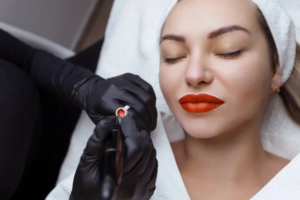 Kosmetolog robi makijaż na twarzy kobiety. Specjalista stosuje tatuaż na ustach pacjenta zbliżenie — Zdjęcie stockowe