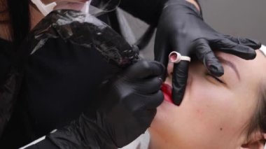 Kozmetik uzmanı bir kadının yüzüne kalıcı makyaj yapıyor. Uzman, hastaların dudaklarına yakın plan dövme uygular.