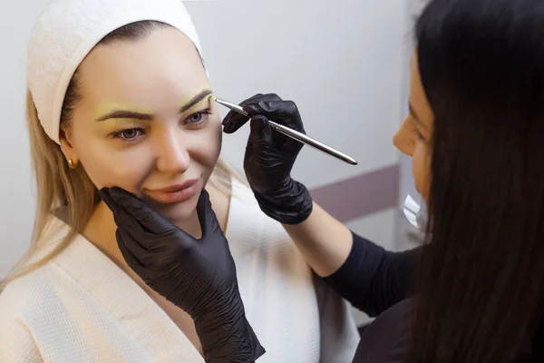 The hand of a make-up artist in black gloves applies a yellow eyebrow paste to the eyebrow. Professional stylish permanent makeup, eyebrow tinting. Close up.