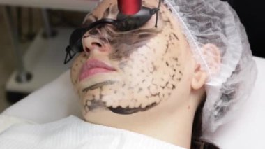 Güzellik uzmanı güzel bir kadının yüzüne siyah maske takıyor. Spa salonundaki muhteşem kadın yüz için karbon soyma işlemi yapıyor..