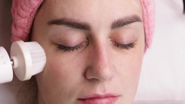 Jonge vrouw schoonmaken gezicht met behulp van cosmetische gezichtsborstel. Gezichtsbehandeling. Cosmetische ingrepen. cosmetologie — Stockvideo
