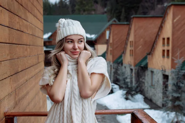 Retrato de uma menina bonita em um chapéu branco e suéter na rua na varanda. Roupas quentes de inverno — Fotografia de Stock